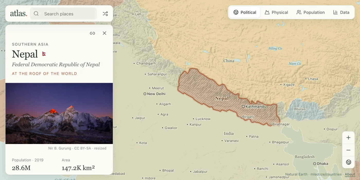 Atlas open on Nepal: the country hatched on a shaded-relief map, with its card and a photograph of the Himalaya beside it.